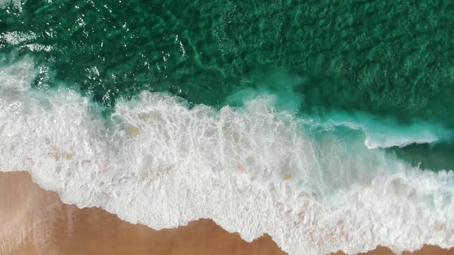 Aerial view of drone flying above beautiful beach with views of ocean waves and water crashing on to sandy beach from top angle