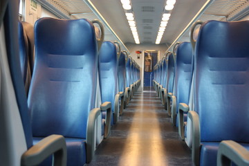 blue lined seats lined up along the corridor of a regional train with no passengers during the day