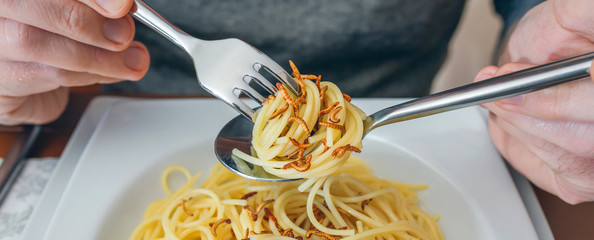 Detail of hands of unrecognizable man eating spaghetti with crispy worms