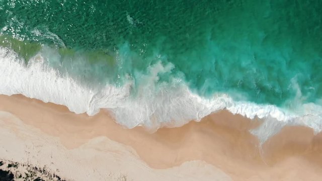 Aerial view of drone flying above beautiful beach with views of ocean waves and water crashing on to sandy beach from top angle