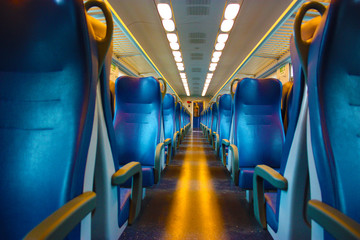 blue lined seats lined up along the corridor of a regional train with no passengers during the day