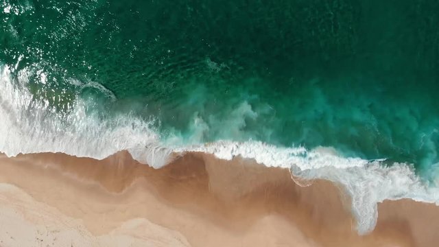 Aerial view of drone flying above beautiful beach with views of ocean waves and water crashing on to sandy beach from top angle