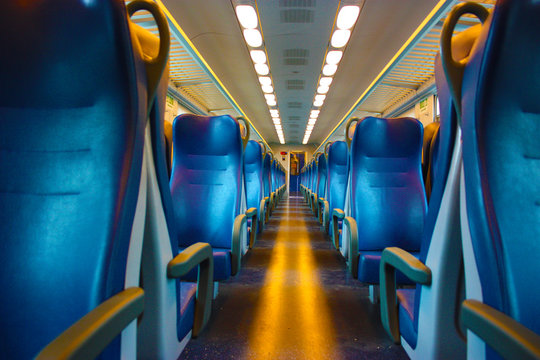 blue lined seats lined up along the corridor of a regional train with no passengers during the day