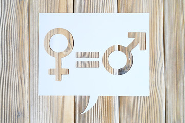 male and female symbols and an equal sign in white dialogue box cut out of paper on a wooden...
