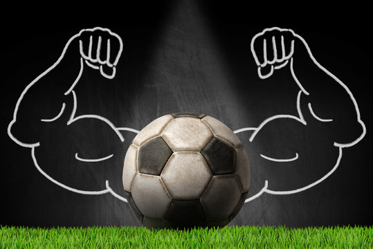 Old leather soccer ball on a blackboard with muscular arms, green grass and copy space