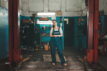 Fototapeta na wymiar Gender equality. A young brunette woman in uniform, standing against the background of a car repair shop. Horizontal