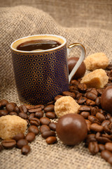 A Cup of coffee, coffee beans, pieces of brown sugar and chocolate on a background of rough homespun fabric. Close up.