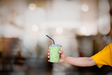 Green tea with mill plastic glass in hand with blurred cafe background.