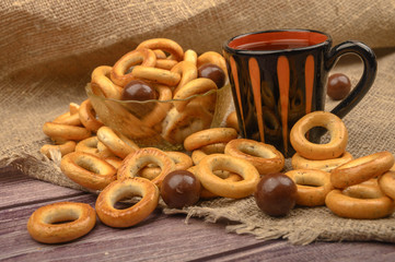 Small bagels, chocolates, a mug of tea and a rough homespun cloth on a wooden background close-up.