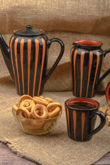 Small bagels, a mug of tea and ceramic dishes on a background of rough homespun fabric close-up.