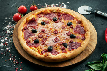 Pizza with a large number of toppings: hunting sausages, onions, mushrooms, salami, cheese and bell pepper. Pizza in composition with ingredients on a black background
