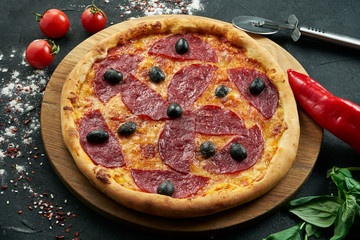 Pizza with a large number of toppings: hunting sausages, onions, mushrooms, salami, cheese and bell pepper. Pizza in composition with ingredients on a black background