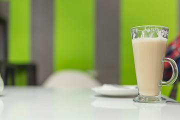 Latte coffee in a tall glass, against the window. Photographed close-up.