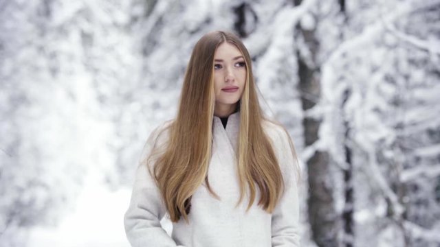 Beautiful woman in winter forest. Young elegant lady in trendy white coat. Fashion winter lookbook. Winter snow-covered forest