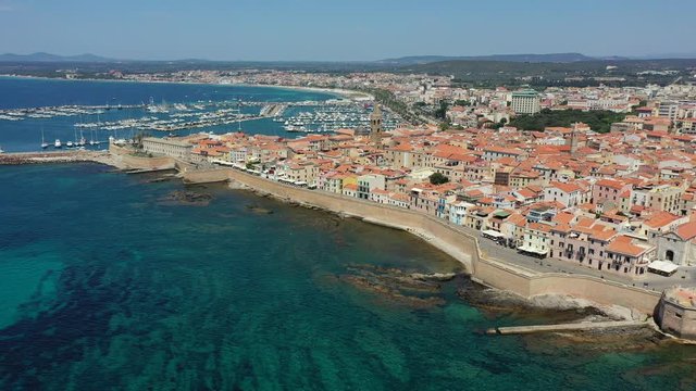 Aerial shot over Alghero old town, cityscape view on a beautiful day with harbor and open sea in view. Alghero, Italy. Panoramic aerial view of Alghero, Sardinia, Italy.