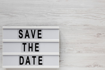 'Save the date' words on a lightbox on a white wooden background, top view. Overhead, from above, flat lay. Space for text.