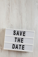 'Save the date' words on a lightbox on a white wooden surface, top view. Overhead, from above, flat lay. Copy space.