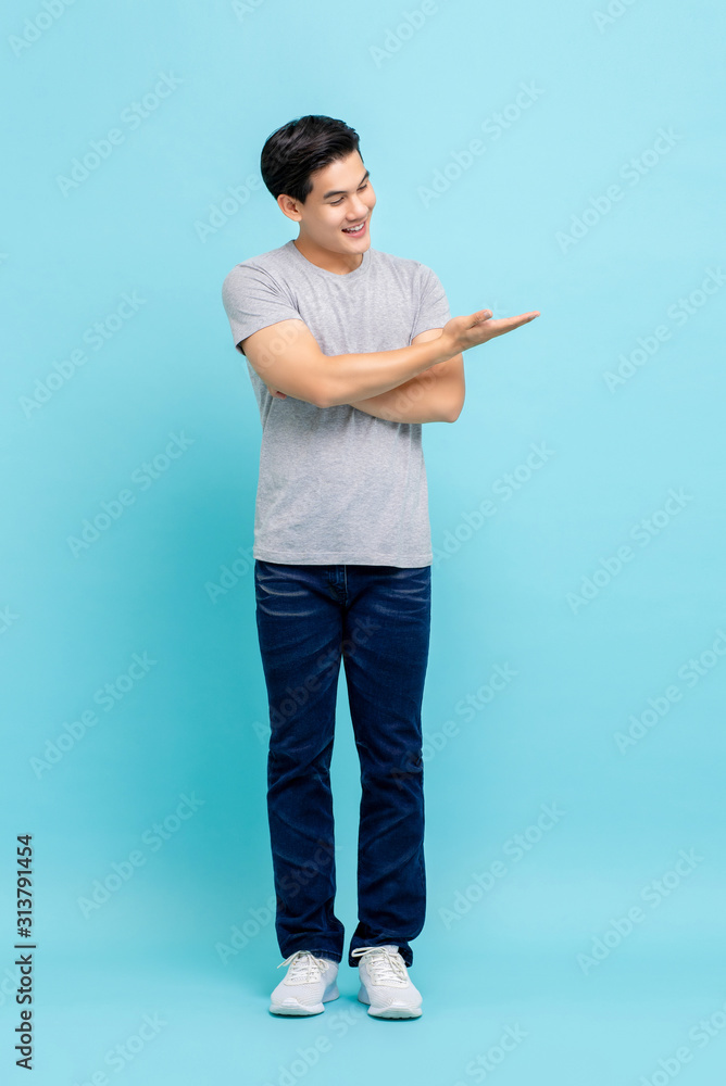 Wall mural asian man in casual clothes smiling and holding out hand with palm open