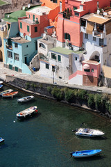 Fishing boats and the promenade in Corricella on Procida, Italy, with the vibrantly colorful houses...