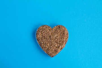 Flax seeds in the heart shape in the center of  the blue background. Top view. Copy space.