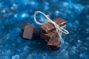 Dark porous chocolate with nuts on the table, closeup. Dark blue trend background 2020. In the background is red chili pepper.