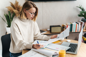Photo of serious attractive woman examining documents and using laptop