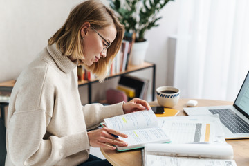 Photo of woman making notes in exercise book and using laptop