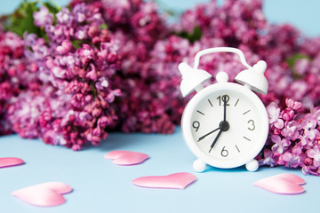 Lilac flowers with vintage tiny alarm clock on blue background. Spring time morning concept.