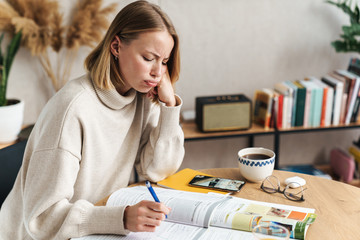 Photo of sad attractive woman making notes in exercise book