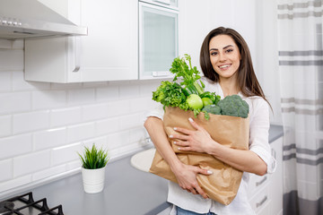 Portrait of young brunette housewife with paper bag full of greengrocery in a kitchen