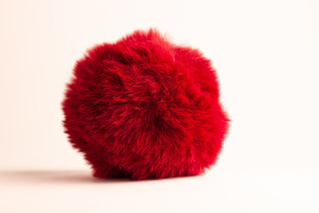 Red fur ball isolated on white background with natural shadow. Keychain, hats fashion style accessory, bag and backpack decoration. Girl clothes wardrobe,female style. Copy space.