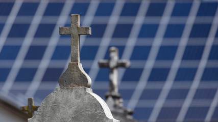 Stone crosses on graves with blurred solar panels in the background