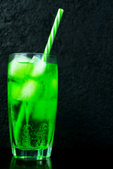 Green tarragon drink with ice on a black background. Cooling drink.