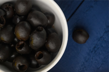 Black olives in a plate on a blue texture closeup