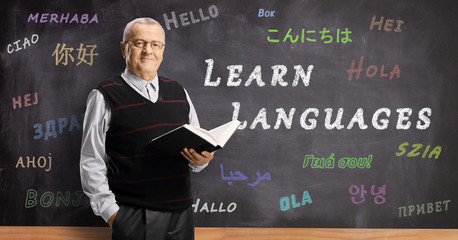 Mature male teacher in front of a blackboard with hello written in different foreign languages