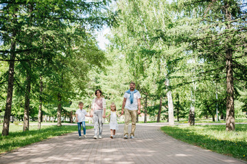 Big happy family with two kids walk in the park shot from distance.