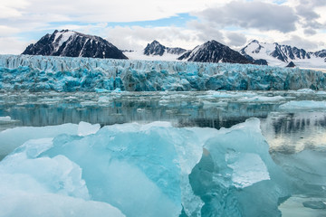 Fototapeta na wymiar Gletscher mit blauem Eis spiegelt sich im Meer, Berge im Hintergrund