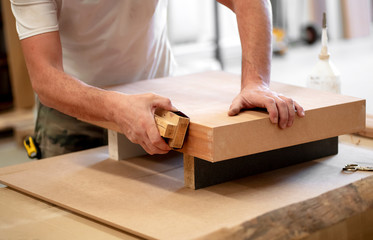 Hands of a carpenter sanding the edge of a block
