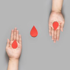 Blood donation - Human hand giving blood drop symbol to a hand on gray background. World blood...