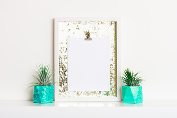 Lifestyle home decoration with frame and place for text. Marbled geometric succulent planters with beautiful tiny succulent plants on white shelf against white wall.