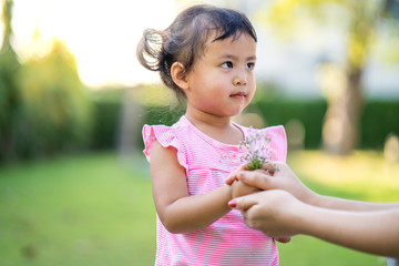 Cute little girl give flower to her mother in garden.