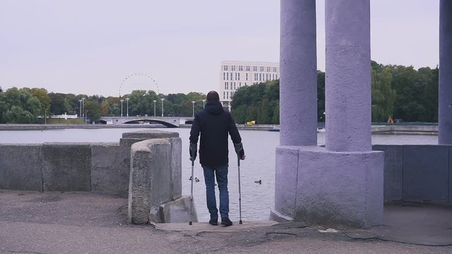 Image of a man with crutches walking on the waterfront of the city