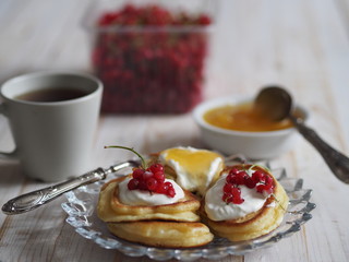 Fritters with sour cream and red currants. Therapeutic tea for colds with honey on a wooden white rustic table. Home kitchen.
