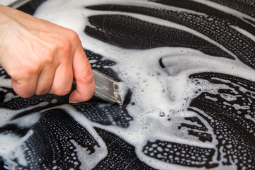 A woman cleans the electronic ceramic hob, using special steel scraper and detergent agent, applied to the surface of the hob. Chores and domestic labour concept.