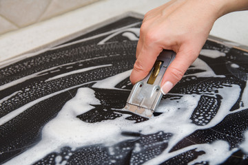 A woman cleans the electronic ceramic hob, using special steel scraper and detergent agent, applied...