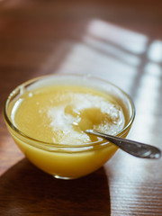 Round glass bowl with honey and spoon on a sunny table