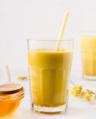 golden milk in a glass with a straw on a white background next to honey. Traditional indian drink