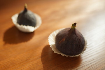 Two ripe sweet figs in white paper on a wooden table.