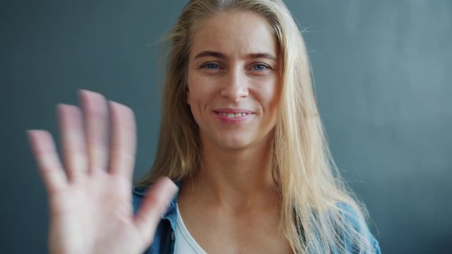 Slow motion of attractive blond woman waving hand smiling on dark background greeting welcoming people. Gestures, communication and friendly people concept.