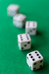 Top view of dice with the number six in the foreground focused, and four dice out of focus in the background on green mat, vertically